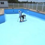 Empty swimming pool with two painters applying blue chlorinated rubber paint with rollers