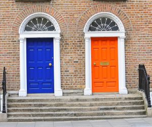 Two brightly painted neighbouring Georgian doors in brick building one is bright blue and the other orange. Steps lead up to both